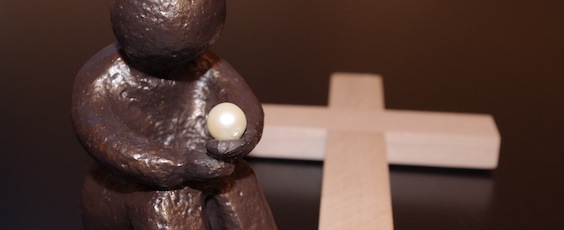 sitzende Skulptur vor Kreuz